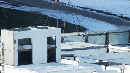 Crane operation lifting prefabricate concrete wall panel for winter building construction project at outdoor site covered with snow and ice