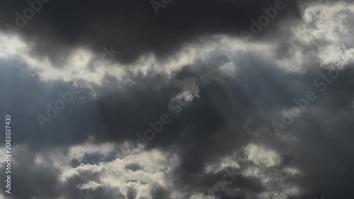 Bright sun rays breaking through dark dramatic storm clouds in sky.