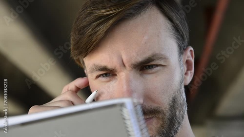 Handsome bearded man looking and sketching in paper notebook close up.