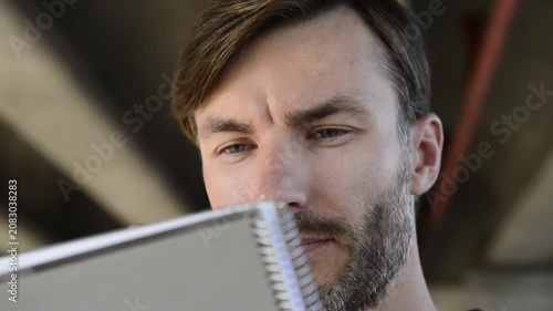 Handsome bearded man looking and sketching in paper notebook close up.