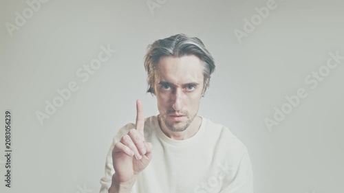 Middle-aged man raising index finger in warning gesture, looking at camera in studio, wearing light sweater against neutral background, communication and caution concept