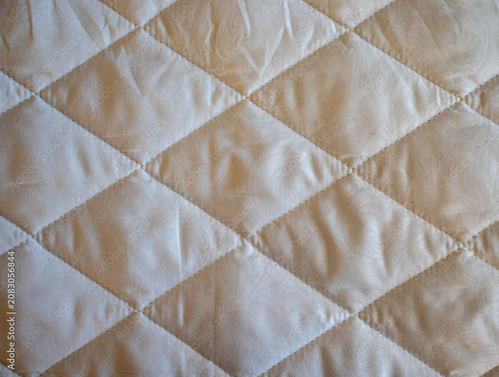 Fototapeta premium Beige quilted fabric texture with a geometric diamond pattern. Ideal backdrop for bedding catalogs, home textile website banners, or mattress manufacturing blogs.