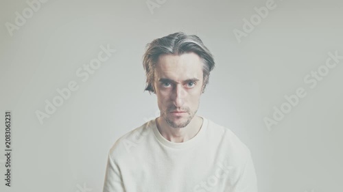 Serious young man with medium-length messy hair in light shirt, intense direct gaze and contemplative expressions, neutral background portrait for introspection and mental health