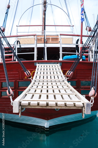 фотографія A wooden gangplank provides access to the stern of a vibrant red sailboat floati