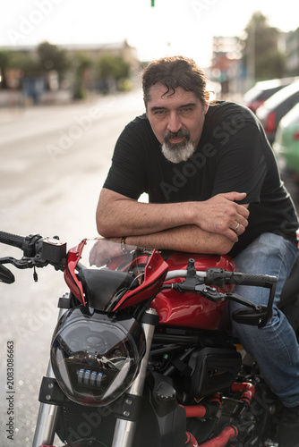 Bearded Man Leaning on Red Naked Motorcycle at Golden Hour
