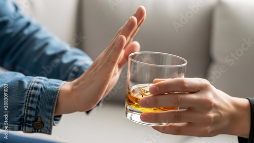 Close-up of a person refusing a glass of whiskey with a hand gesture in a social setting emphasizing moderation and responsible drinking habits