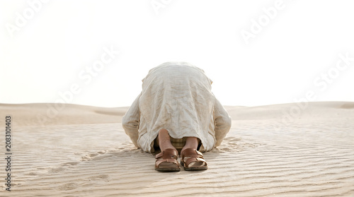 Man in traditional robe prostrating in prayer on desert sand dunes