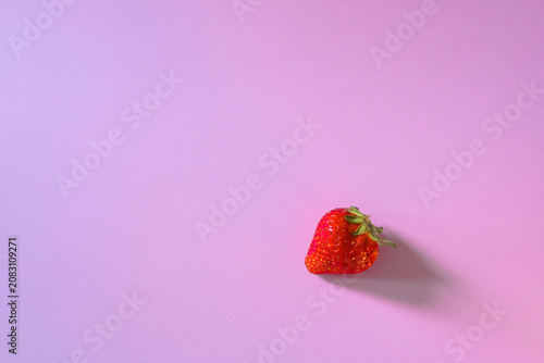 Minimalist food styling of one organic sweet strawberry on clean violet background with graphic shadow