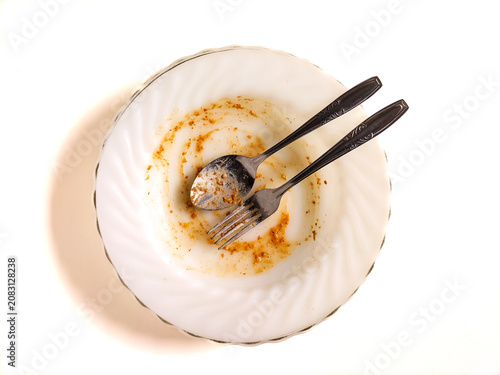 Empty white plate with leftover sauce stains, spoon, and fork after a finished meal, isolated on a white background. Representing satisfaction, delicious taste, or food waste concepts.