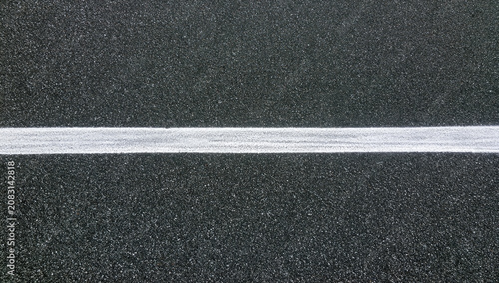 Fototapeta premium A stark white line divides a textured dark gray asphalt surface