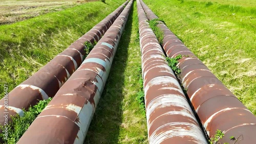 Aerial view of industrial pipes for gas, water, and oil running parallel across a green landscape, showcasing their weathered surfaces and surrounding vegetation in a natural setting