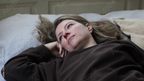Принти на полотні Middle aged woman lying on a bed in an emotionally withdrawn pose with a depressed expression