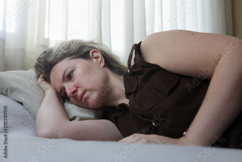 Принти на полотні Sad middle aged woman lying on a bed in an emotionally withdrawn pose with a depressed expression