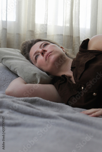 Tableau sur toile Middle aged woman lying on a bed in an emotionally withdrawn pose with a depressed expression