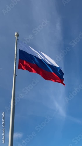 Russian flag waving in the wind on a tall flagpole against a blue sky. national symbol, patriotism, outdoors.