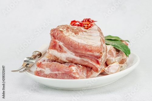 Raw pork ribs with garlic, spices and bay leaves on a white ceramic plate with a meat fork