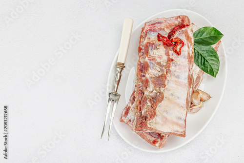 Raw pork ribs with garlic, spices and bay leaves on a white ceramic plate with a meat fork