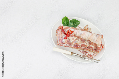 Raw pork ribs with garlic, spices and bay leaves on a white ceramic plate with a meat fork