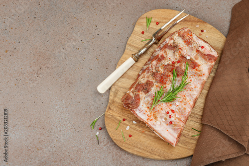 Raw marinated pork ribs with rosemary, spices and garlic on a wooden cutting board with a meat fork