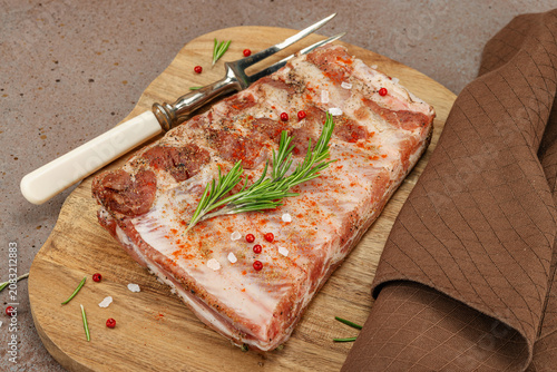 Raw marinated pork ribs with rosemary, spices and garlic on a wooden cutting board with a meat fork