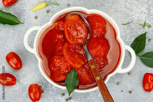 Canned whole peeled tomatoes in tomato juice in a white ceramic bowl with spoon. Rustic food styling