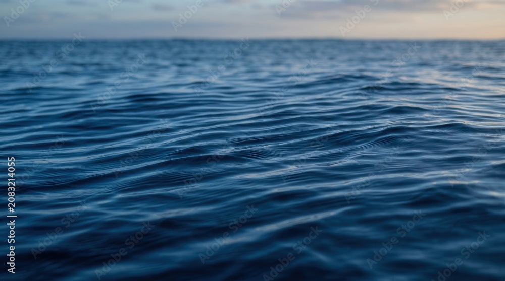 Naklejka premium Deep blue ocean water with gentle ripples on the surface. Soft evening sky on the horizon in the background.