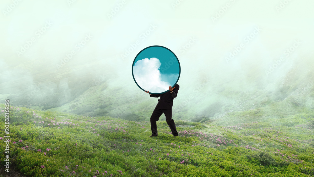 Naklejka premium Businessman carrying round sky mirror in misty green landscape. Concept of clear vision, future planning, creative leadership, sustainability strategy, fresh perspective.