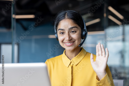 Photography Close-up photo of a young Indian woman in a suit sitting at an office desk talki