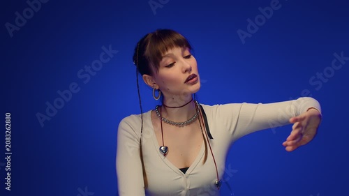 Serious young woman blue studio lifting arm and looking forward with calm fashion portrait mood pose