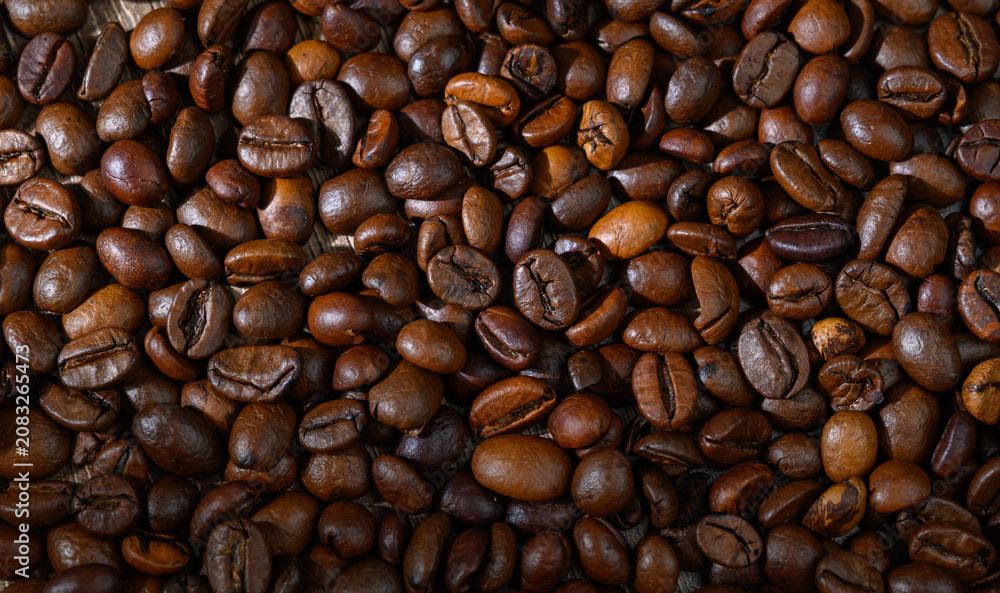 Obraz premium Rich and aromatic roasted coffee beans scattered on a wooden surface showcasing their deep, earthy hues