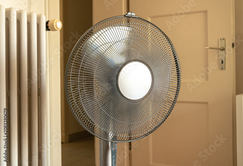 Electric metal pedestal fan in a home interior with blurry background