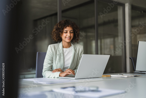 Young professional specialist latin hispanic businesswoman in suit working on laptop pc sitting at desk in office. Middle eastern indian woman using computer technology app for work online. Copy space