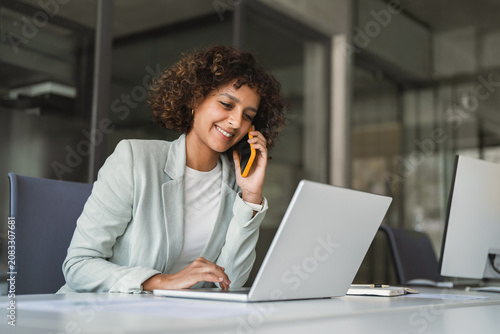 Foto Young Indian woman manager ceo using cell phone mobile, laptop for business call