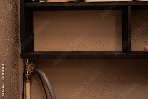 A shelf is shown in a room with pipes. The shelf has empty spots and some items