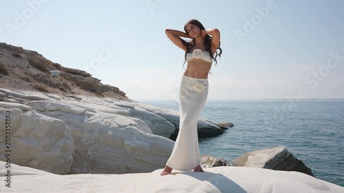 Beautiful young woman posing gracefully on white rocks by the sea