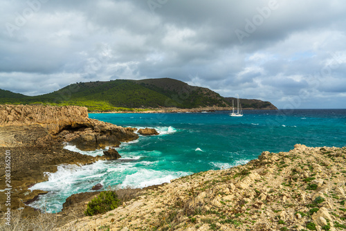 White sailing yacht with lowered sails drifting near coast of Mallorca, Spain. Calm Mediterranean Sea, luxury boating, summer travel, leisure and seaside vacation concept.