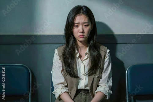 Worried Young Korean Woman Sitting Alone in Dimly Lit Room with Dramatic Shadows
