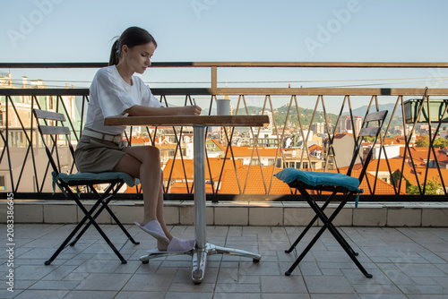 teenage student studies at a rooftop terrace table during a city trip, combining distance learning, travel accommodation and a quiet morning study routine with a skyline view