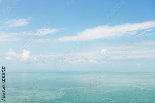 calm black sea horizon beneath a soft blue sky with white clouds, creating an airy coastal background for summer travel, wellness, relaxation and peaceful escape concepts