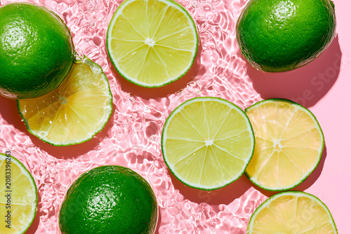 Fresh Limes Floating in Crystal Clear Water on Pastel Pink Background with Sunlight Ripples