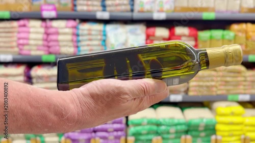 Male Hand Holding a Bottle of Vegetable Oil in Front of Shelves with Various Cooking Oils in a Supermarket