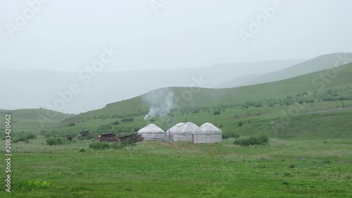 Traditional yurts with smoke rising from a chimney in the misty green mountains of Central Asia. Commercial background for travel, nomad culture, and authentic lifestyle concepts.