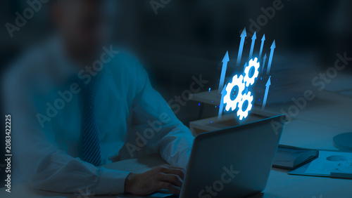 Businessman Working on Laptop with Glowing White Gear Icons and Upward Blue Arrows, Business Growth, Automation, Digital Transformation, Technology Process, Ai Innovation on Dark Background