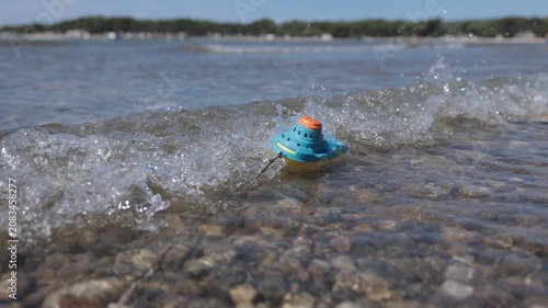A small toy boat struggles against incoming waves before tumbling in the surf, creating a powerful visual metaphor for fragile childhood dreams challenged by life's obstacles. Slow-motion water