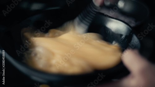 Cinematic close up of whisking and scrambling eggs with a spatula in a hot frying pan.