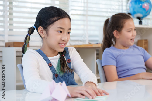 Photography Asian preteen girl and caucasian girl sitting together during classroom origami