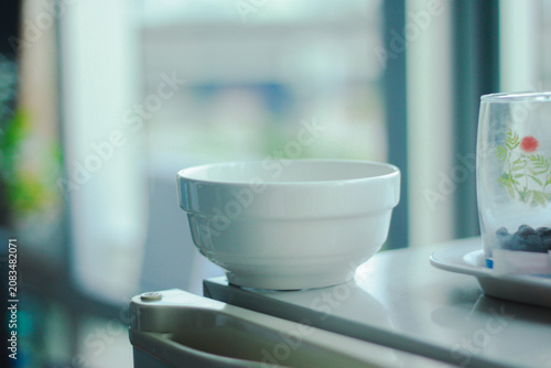 A minimalist white ceramic bowl placed on a digital kitchen scale beside a clear glass, illuminated by soft natural window light. A clean, modern kitchen scene with a calm atmosphere, perfect for food