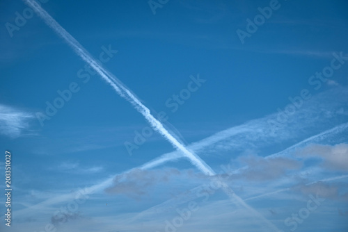 Plane trail and white clouds in the blue sky. Chemtrail conspiracy theory.