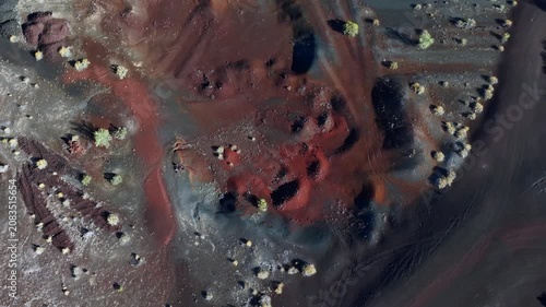 An aerial top-down drone shot pulling up to reveal abstract volcanic textures, red iron oxide soil, and dark basalt ash fields with sparse desert vegetation in El Pinacate Biosphere Reserve, Mexico.