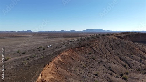 A scenic wide aerial drone shot tracking along the massive ridge of El Colorado volcanic crater, revealing the vast desert plains, distant mountains, and an expedition vehicle on a dirt road in El Pin